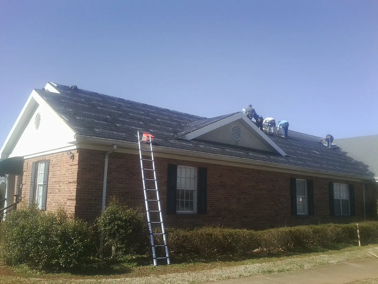 Crew tearing shingles off a brick ranch roof with a ladder set — Emergency Roof Repair work by our crew in Merrimac