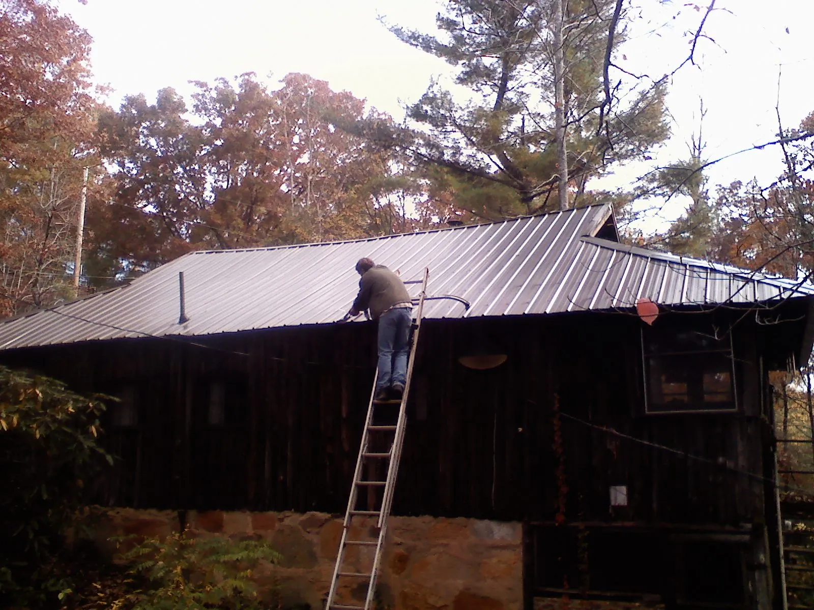 Roofer on a ladder working along the edge of a cabin metal roof in Merrimac