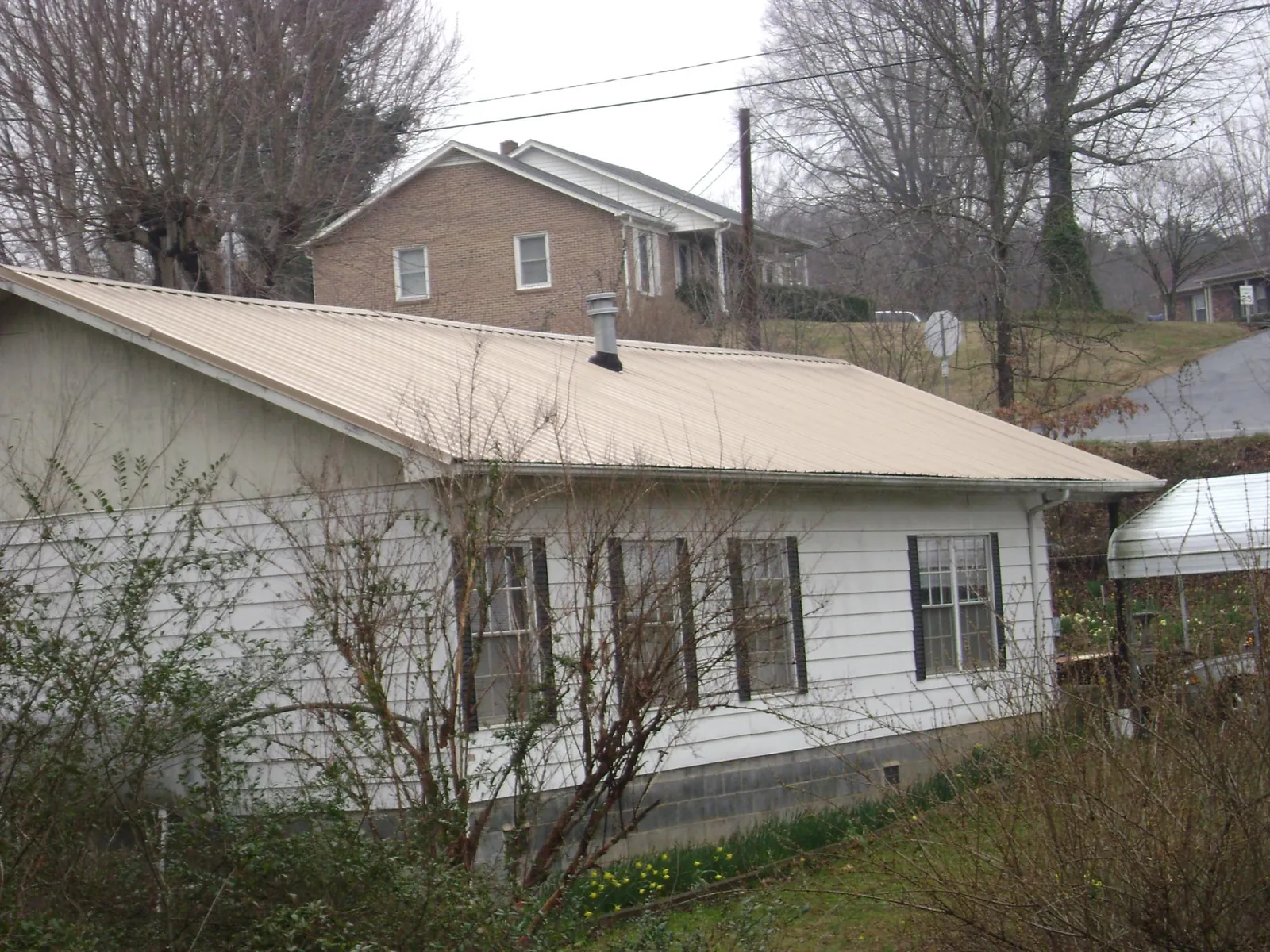 Tan metal roof on a white sided house set into a hillside — Commercial Roofing by Roofing Brothers in Merrimac