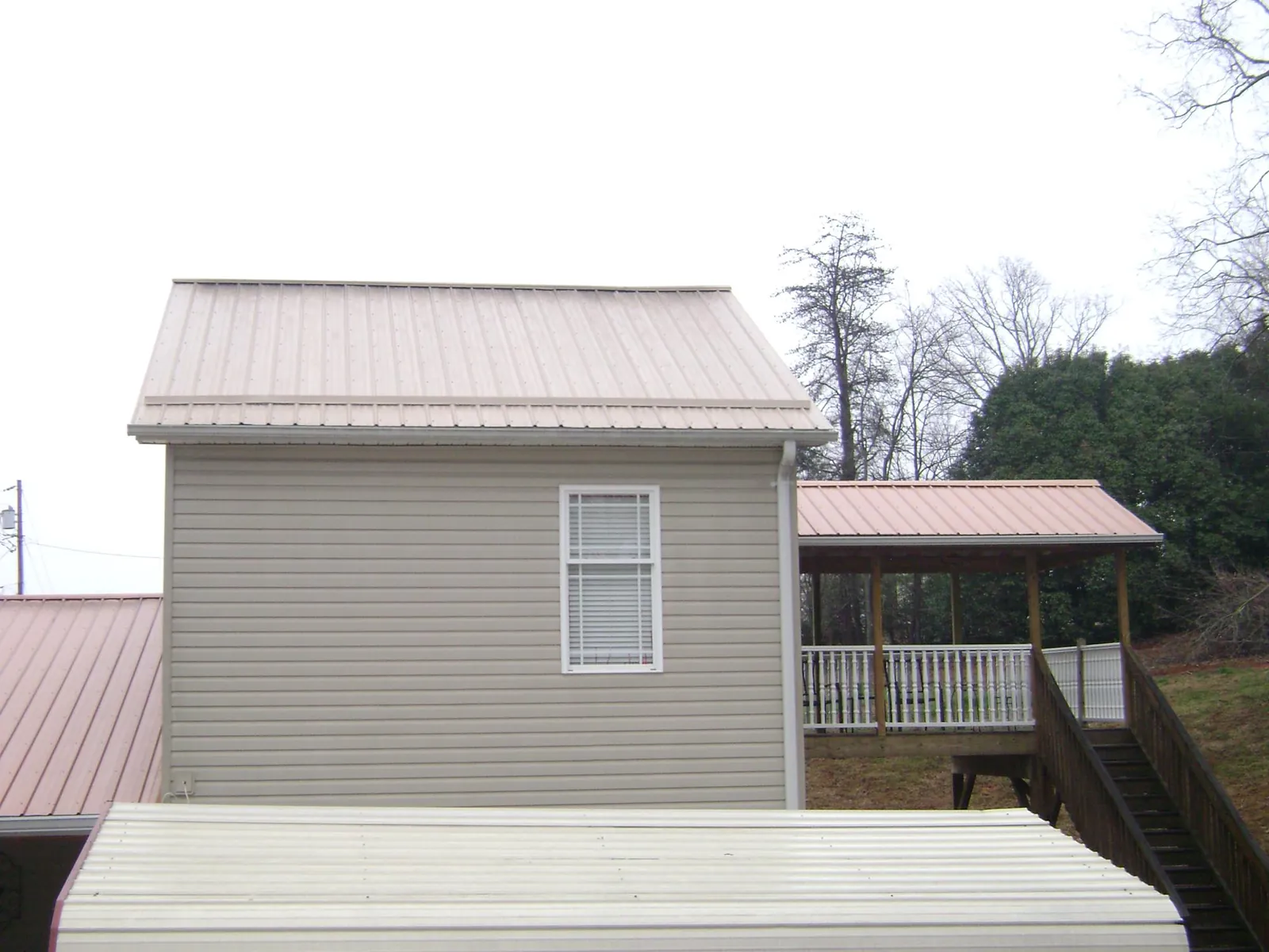 Tan metal roofs on a two story addition and attached porch, from a Roof Replacement job in Merrimac